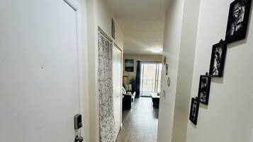Un couloir avec un plancher en bois, des murs blancs et une porte sur le côté gauche. Des tableaux encadrés ornent le mur de droite.