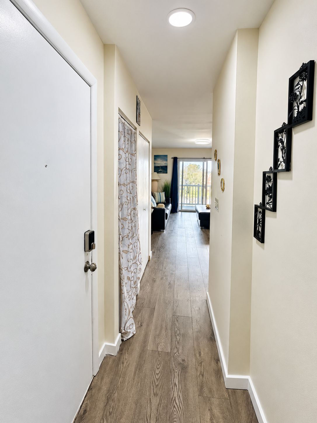 A hallway with a white door, a patterned curtain, and a view to a balcony.