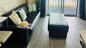 Una sala de estar moderna con un sofá de cuero negro, piso de madera, una mesa de comedor y vistas a un balcón con barandilla.