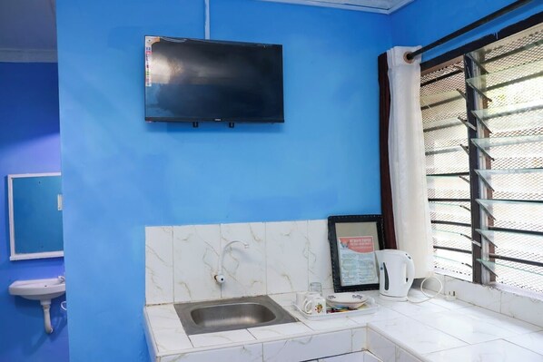 A bathroom with a blue wall, a white sink, a mirror, a toilet, and a window with metal bars. - Mtwapa Empire Holiday Apartments (Mtwapa)