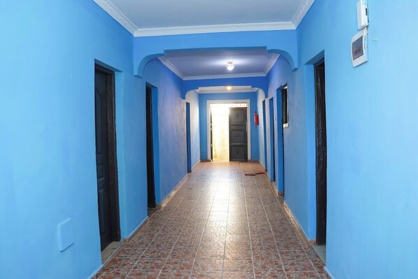 Un pasillo con paredes azules y piso de baldosas, que conduce a una puerta al final.