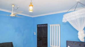 A room with blue walls, a ceiling fan, a bed with a canopy, and a door with a decorative design. - Mtwapa Empire Holiday Apartments (Mtwapa)