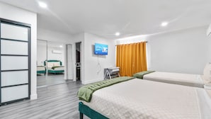 Hotellihuone, jossa on kaksi sänkyä, televisio ja liukuovi, joka johtaa kylpyhuoneeseen.