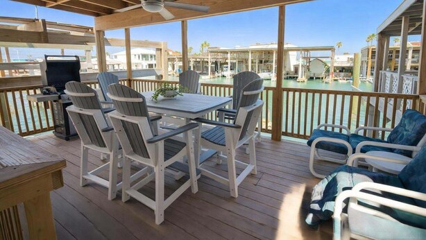 Une terrasse extérieure couverte, dotée d’une table et de chaises, d’un ventilateur de plafond et offrant une vue sur une marina remplie de bateaux.