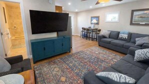 Un salon équipé d’un téléviseur à écran plat, d’un ventilateur de plafond, d’un canapé, d’une table basse et d’un tapis à motifs.