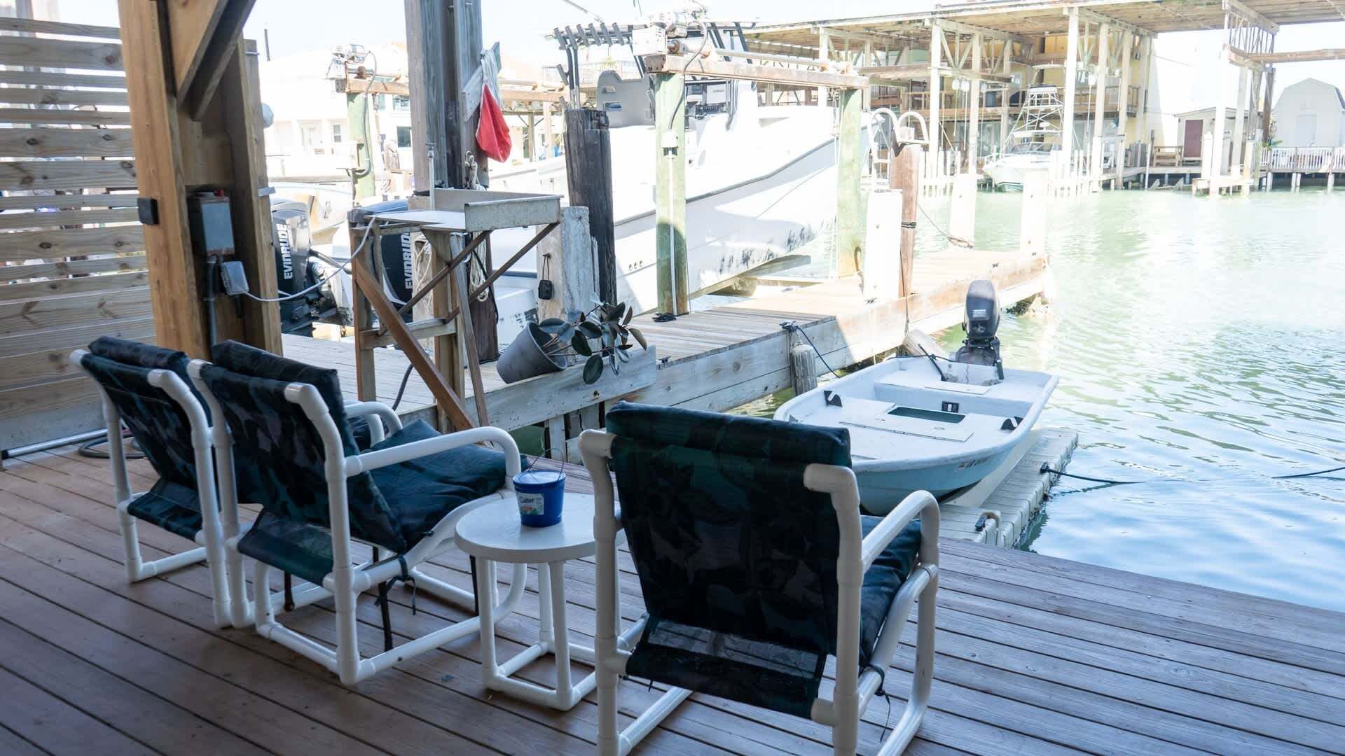 A wooden deck with two rocking chairs and a small table, overlooking a marina with boats docked.