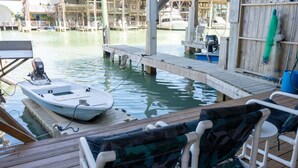 Un quai avec un bateau, des chaises longues en bois et une vue sur une marina avec des bateaux et des bâtiments.
