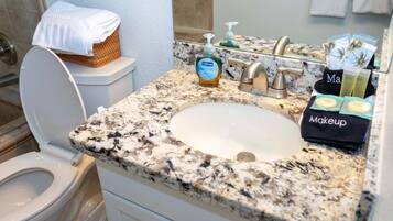 A bathroom with a granite countertop, a white sink, a toilet, and a basket with a towel on the toilet.