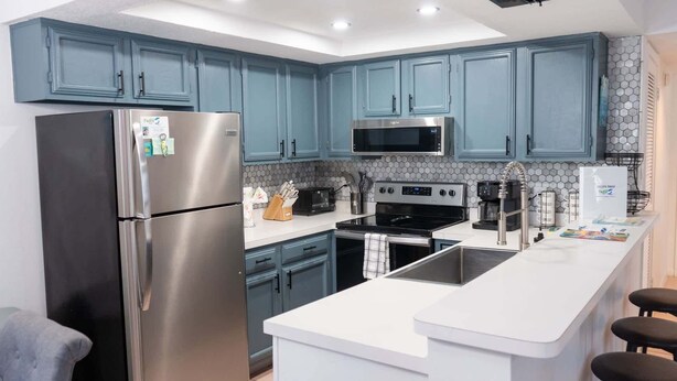A modern kitchen with teal cabinets, stainless steel appliances, and a white countertop. - Walkable Location 99 Steps To Beach Pool 2 Bedroom Apts (South Padre Island)
