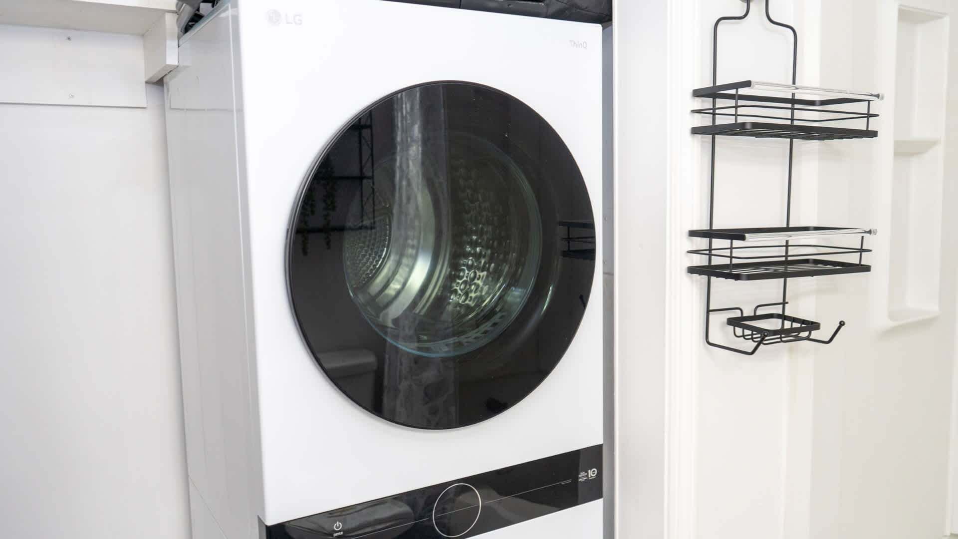 Un lave-linge à chargement frontal doté d’un panneau de commande et d’une étagère en métal noire située à sa droite.