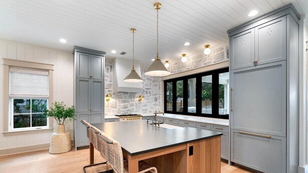 Une cuisine moderne dotée d’un grand îlot central, de meubles de couleur grise et de luminaires suspendus.