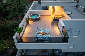 Een modern terras op het dak met een jacuzzi, lounge fauteuils en een eethoek.
