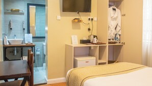 Habitació d'hotel amb un llit, una taula de treball amb cadira, un lavabo, un mirall, una televisió i una bata penjada a una càmera.