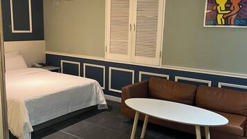 A bedroom with a bed, a brown leather sofa, and a small white table.