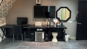 Una moderna camera d'albergo con una scrivania nera, una TV a schermo piatto, un frigorifero compatto, una macchina del caffè e un WC dal design originale.