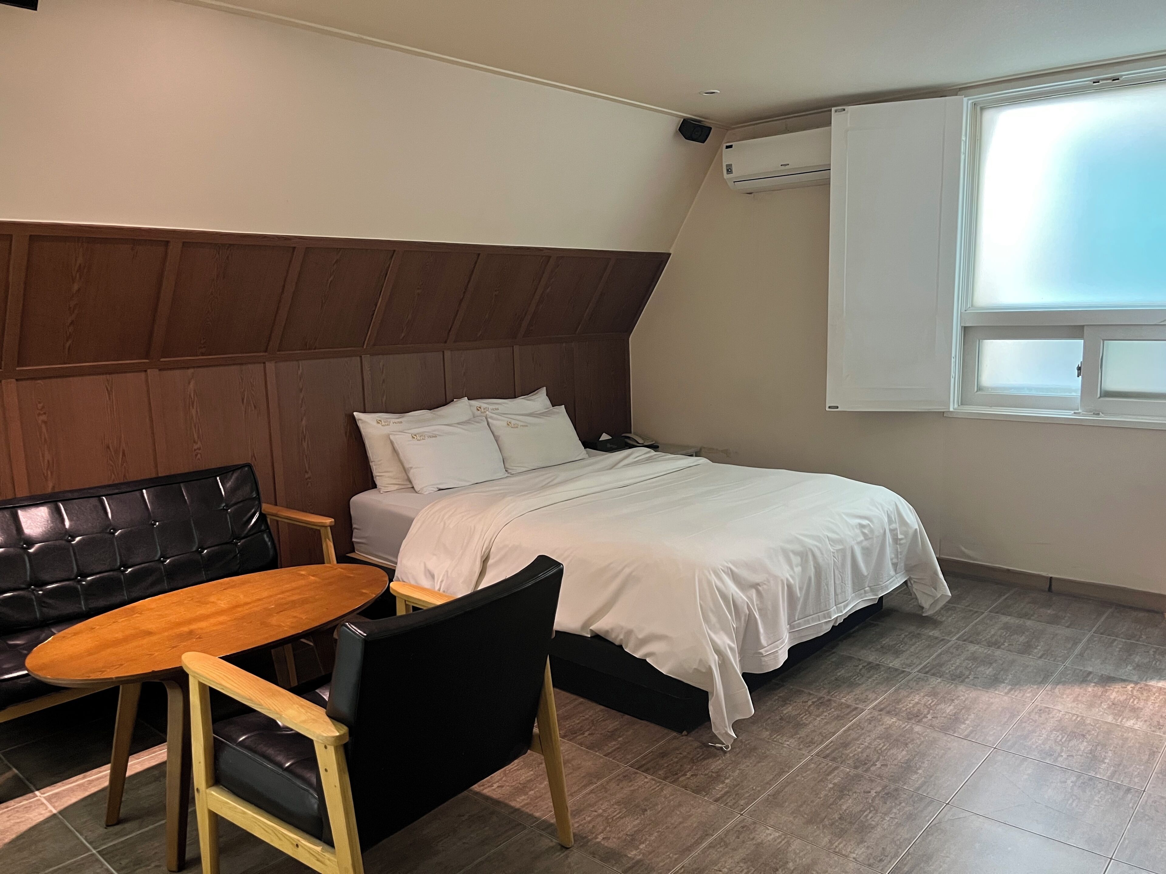 Une chambre à coucher avec un lit, une tête de lit en bois, une petite table et une chaise noire.
