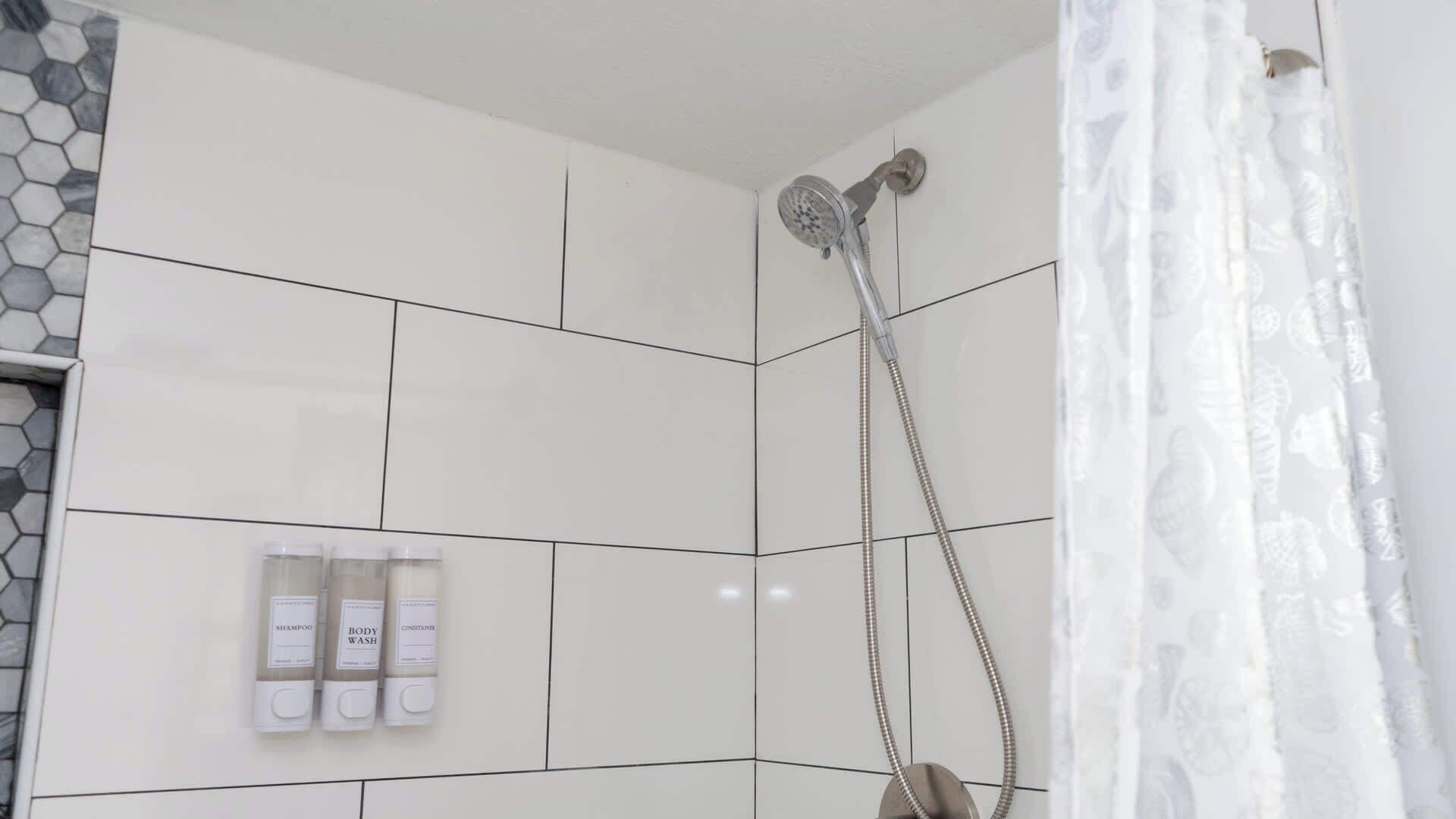 Zona de ducha con pared de azulejos, cabezal de ducha y cortina.