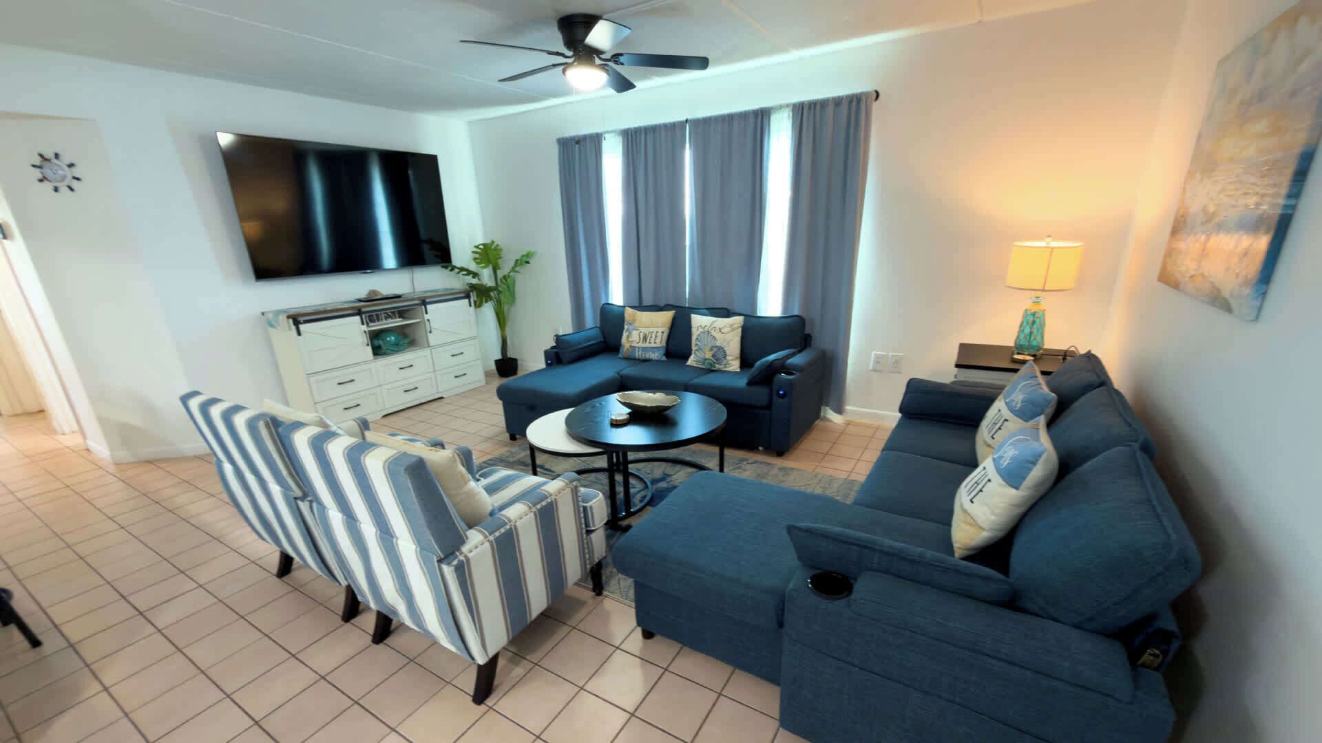 A living room with a sofa, armchairs, a coffee table, a TV, and a ceiling fan.