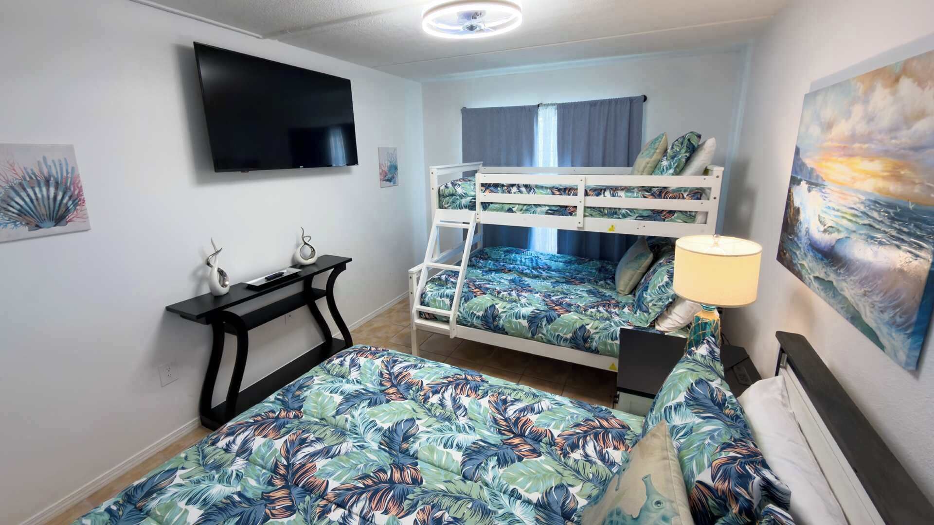 A room with bunk beds, a flat-screen TV, a desk with two decorative items, and a painting on the wall.