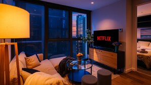 Ein modernes Wohnzimmer mit einer Couch, einem Couchtisch, einem Fernseher und einem großen Fenster mit Blick auf Gebäude.
