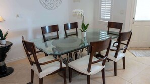 Un espace repas avec une table en verre entourée de chaises en bois dotées de coussins blancs.
