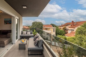 Ein Balkon mit einer Couch und einem Couchtisch, mit Blick auf eine Wohngegend mit Häusern und Bäumen.