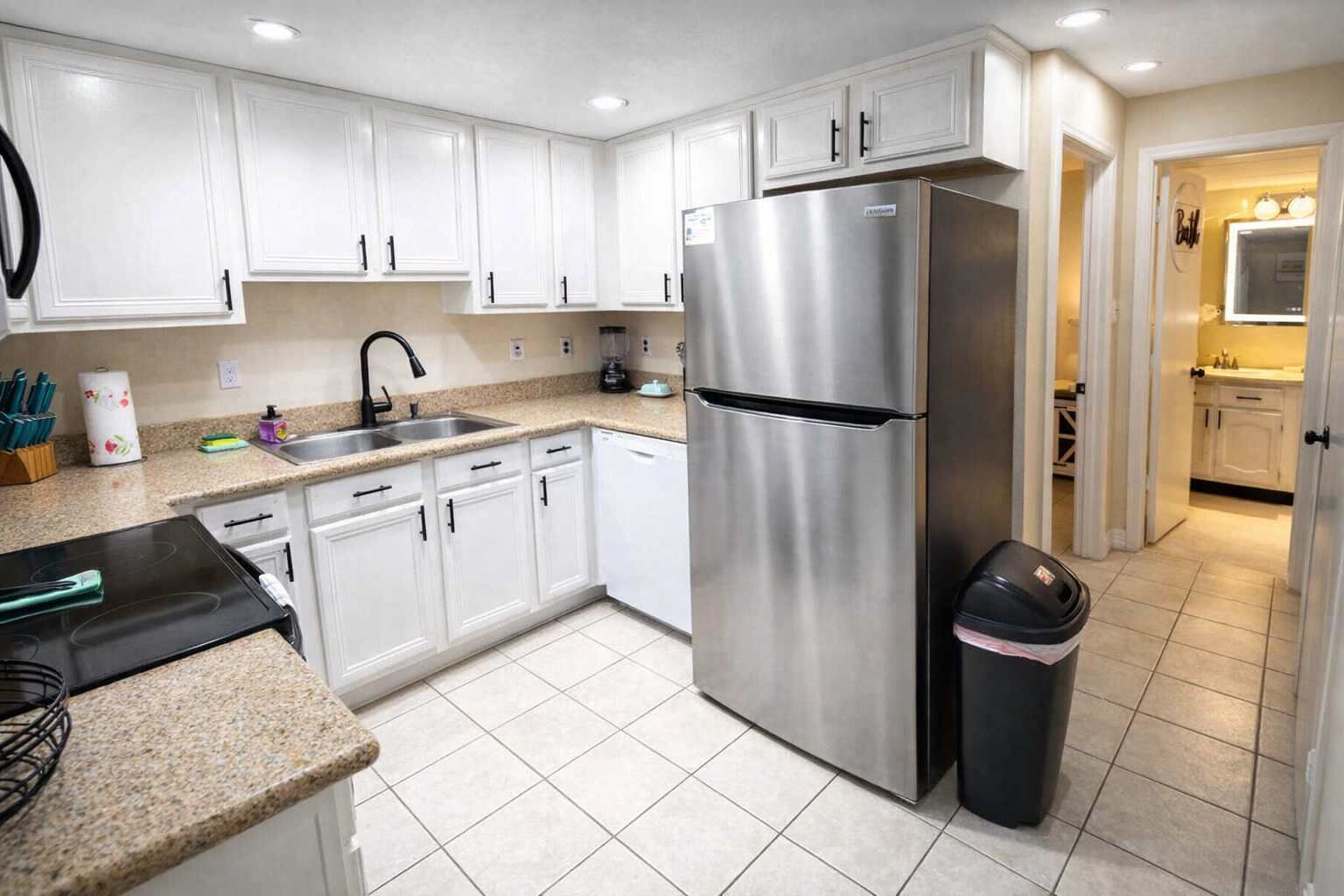 Una cocina moderna con armarios blancos, un refrigerador de acero inoxidable, un lavamanos y un bote de basura.