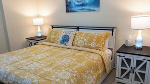 A neatly made bed with a floral bedspread, two bedside lamps, a decorative pillow, and a painting on the wall. - Direct Bayfront Sunsets - Boat Docks - Pool - Fish (South Padre Island)