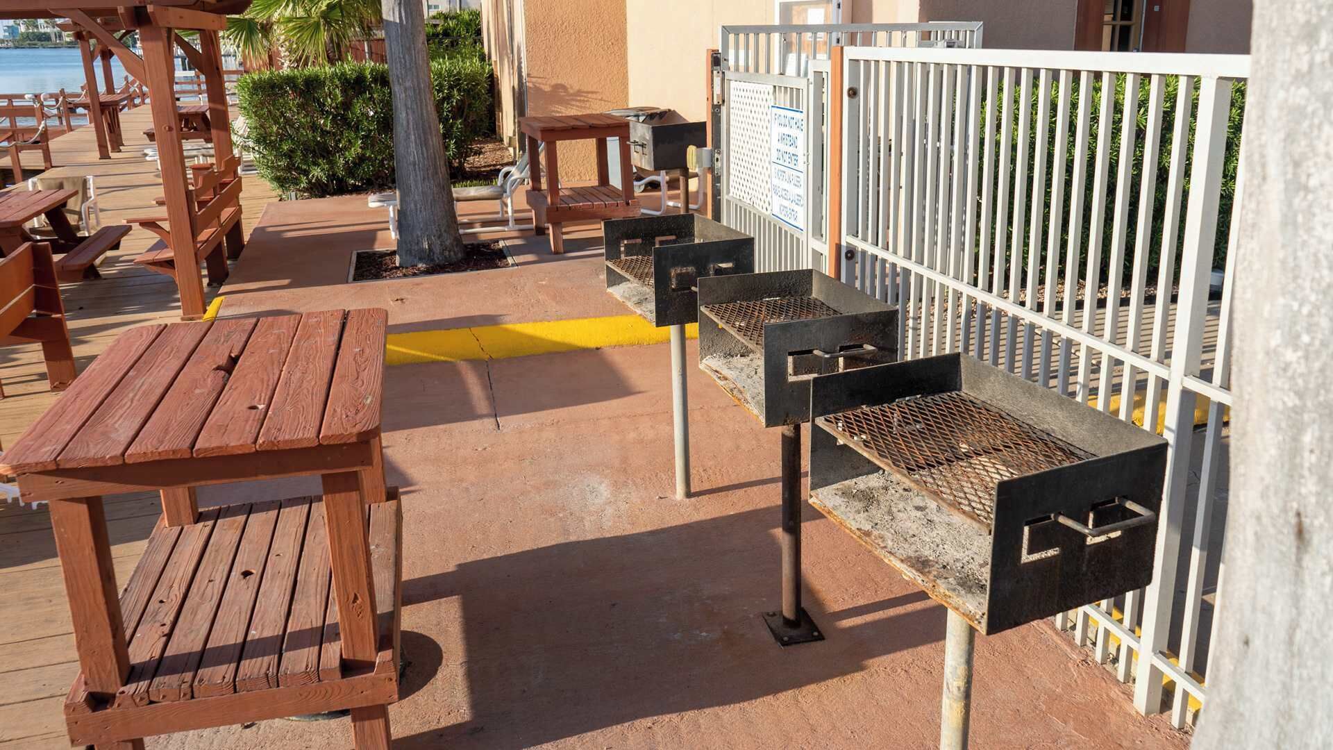 Una terrassa de fusta amb taules de pícnic i barbacoes, tot voltat per una tanca blanca.