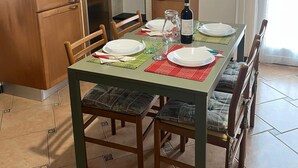Ruokailutila, jossa on neljälle katettu ruokapöytä, puiset tuolit, kaappi ja hyllyllä oleva televisio.