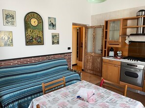 A cozy kitchen with a wooden table, a striped sofa, and a vintage clock on the wall. - Km 54 – 1,200 m from the sea. Free parking. Expenses included. (Moneglia)