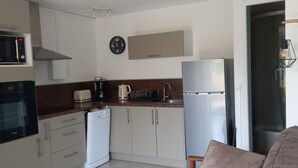 A compact kitchen with a microwave, coffee maker, and refrigerator. There is a clock on the wall and a sofa in the living area. - Cap d'Agde, Garden level Res. Agathe Plus, near Roquille and Mole beaches (Agde)