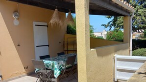 A covered patio with a table and chairs, a door, and a white gate. - Cap d'Agde, Garden level Res. Agathe Plus, near Roquille and Mole beaches (Agde)