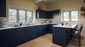 A modern kitchen with dark blue cabinets, a central island, and a window with a view of trees. - Cosy barn in Devon.Set within wonderful countryside- 15 mins from Jurassic coast (Axminster)