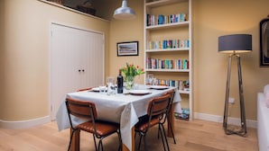 A dining area with a table set for four, surrounded by bookshelves filled with books. - Cosy barn in Devon.Set within wonderful countryside- 15 mins from Jurassic coast (Axminster)