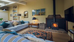 A cozy living room with a sofa, a fireplace, a bookshelf, and a large window. - Cosy barn in Devon.Set within wonderful countryside- 15 mins from Jurassic coast (Axminster)