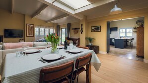 A dining area with a table set for four, a sofa, and a kitchen in the background. - Cosy barn in Devon.Set within wonderful countryside- 15 mins from Jurassic coast (Axminster)