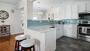 A modern kitchen with white cabinetry, a blue tiled backsplash, stainless steel appliances, and a central island with stools. - Bright and Airy Townhouse in Reserves of Nassau - 17316 King Philip Way (Lewes)