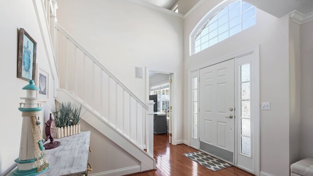 A spacious hallway with a wooden floor, a white staircase, and a door leading to a kitchen area. - Bright and Airy Townhouse in Reserves of Nassau - 17316 King Philip Way (Lewes)