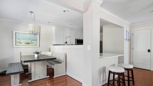 A modern kitchen with white cabinetry, a wooden dining table, and a bar area with stools. - Bright and Airy Townhouse in Reserves of Nassau - 17316 King Philip Way (Lewes)