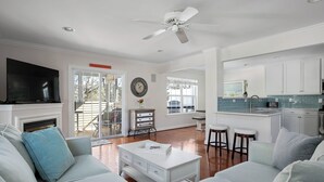 A spacious living room with a white sofa, a coffee table, and a TV. There is a kitchen area with a bar and stools. - Bright and Airy Townhouse in Reserves of Nassau - 17316 King Philip Way (Lewes)
