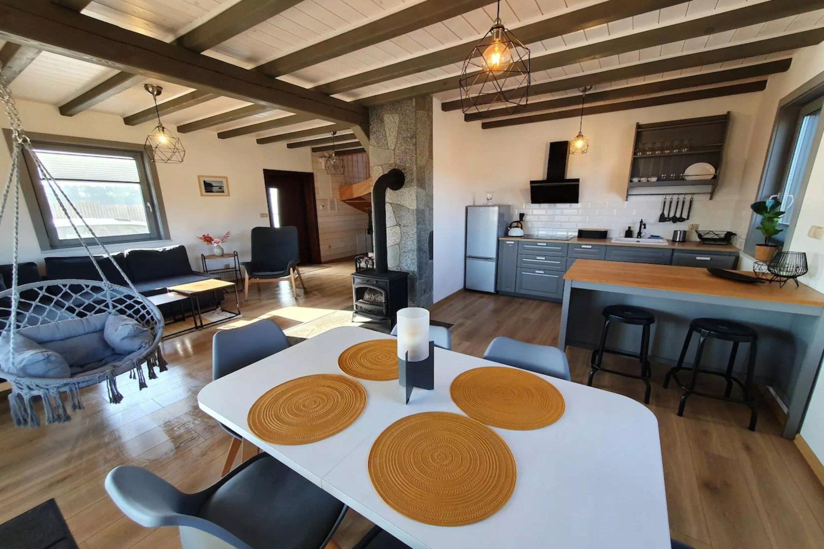 A modern kitchen with a central island, a dining area with a white table and brown placemats, and a cozy seating area with a hanging chair.