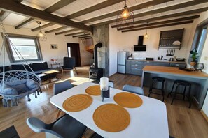 A modern kitchen with a central island, a dining area with a white table and brown placemats, and a cozy seating area with a hanging chair. - Comfortable Holiday Home With a Terrace and Garden (Karsin)