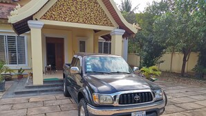 Una camioneta pickup negra Toyota estacionada frente a una casa con fachada amarilla y detalles dorados ornamentales.