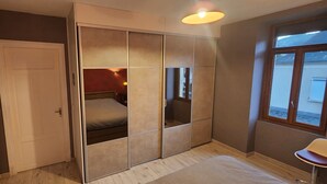 Une chambre avec un placard à portes coulissantes, un lit, une fenêtre et un petit tabouret.