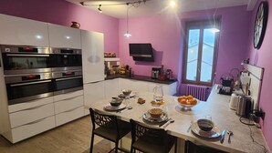 Une cuisine moderne dotée d’appareils électroménagers intégrés, un coin repas avec une table dressée pour deux personnes et une fenêtre laissant entrer la lumière naturelle.
