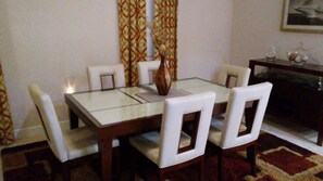 Et spiseområde med et bord med glasplade, hvide stole og en dekorativ vase.