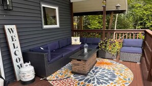 A covered outdoor seating area with a sofa, a coffee table, and a decorative rug. - Private Adirondack Family Retreat. (Moriah)