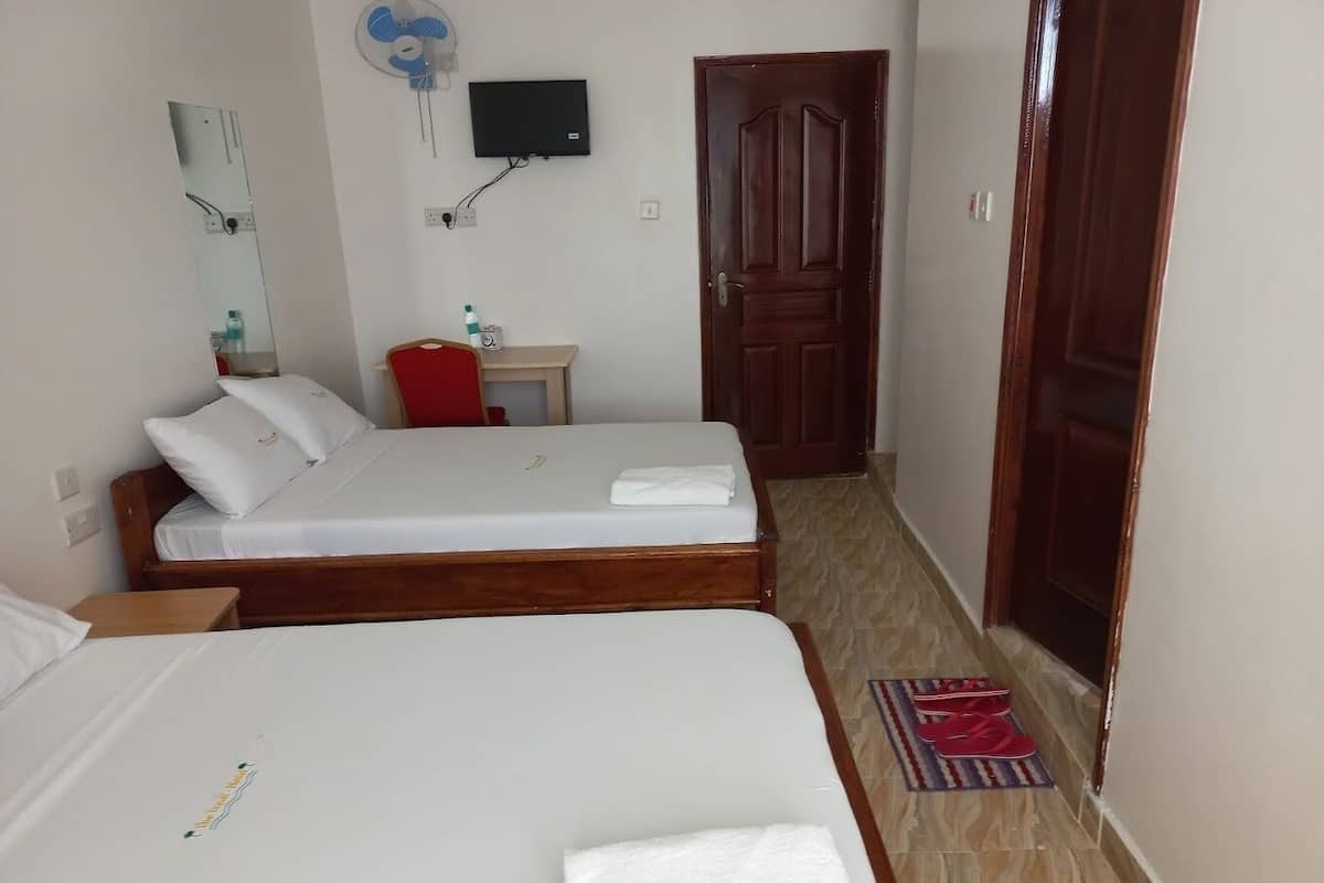 Une chambre d’hôtel avec deux lits, une télévision, un miroir, une petite table et une porte.