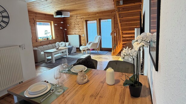 A wooden interior with a dining area, a sofa, and a staircase.